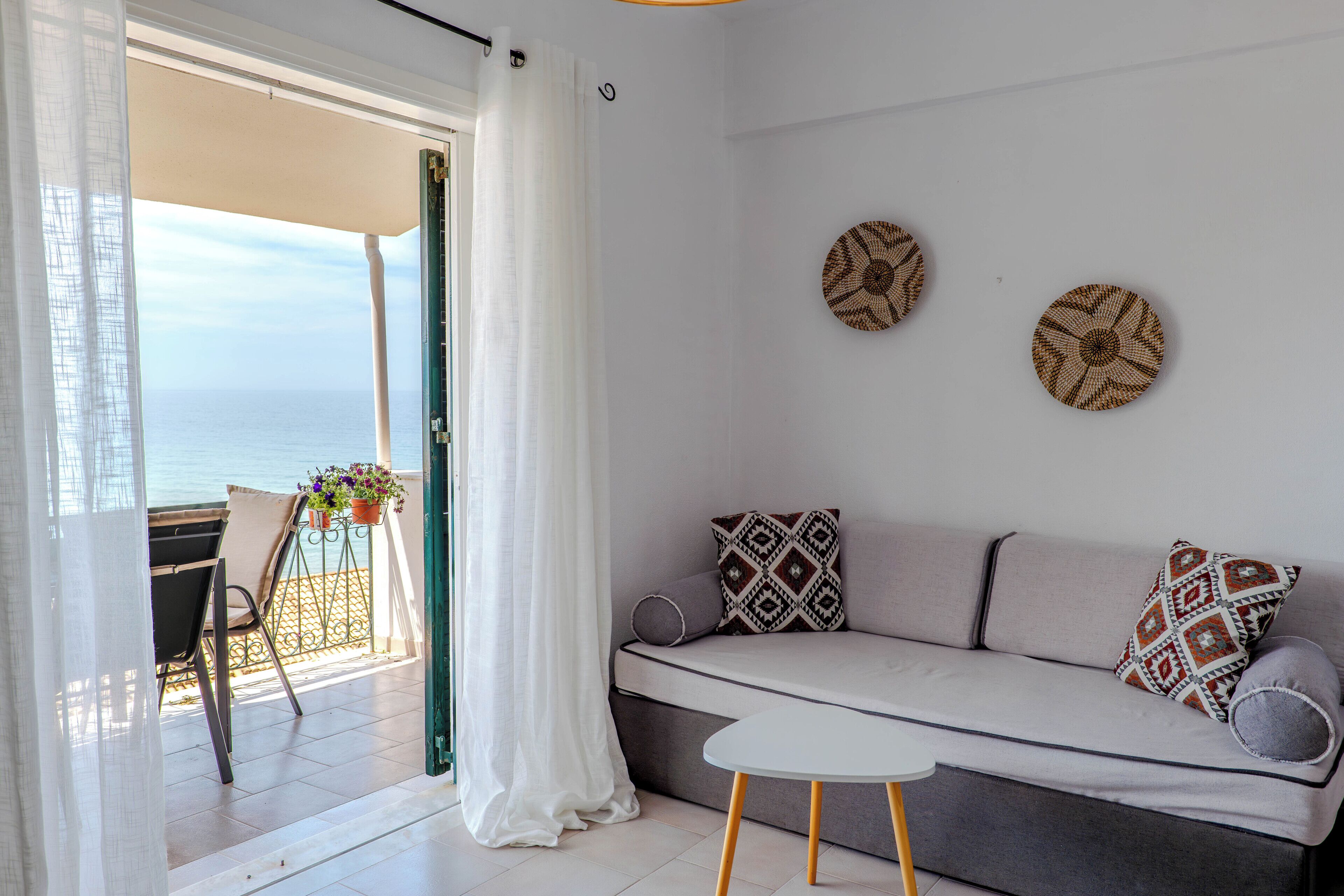 A balcony with a view of the sea, a sofa with patterned cushions, and a small table.