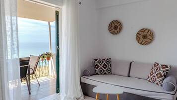 A balcony with a view of the sea, a sofa with patterned cushions, and a small table.