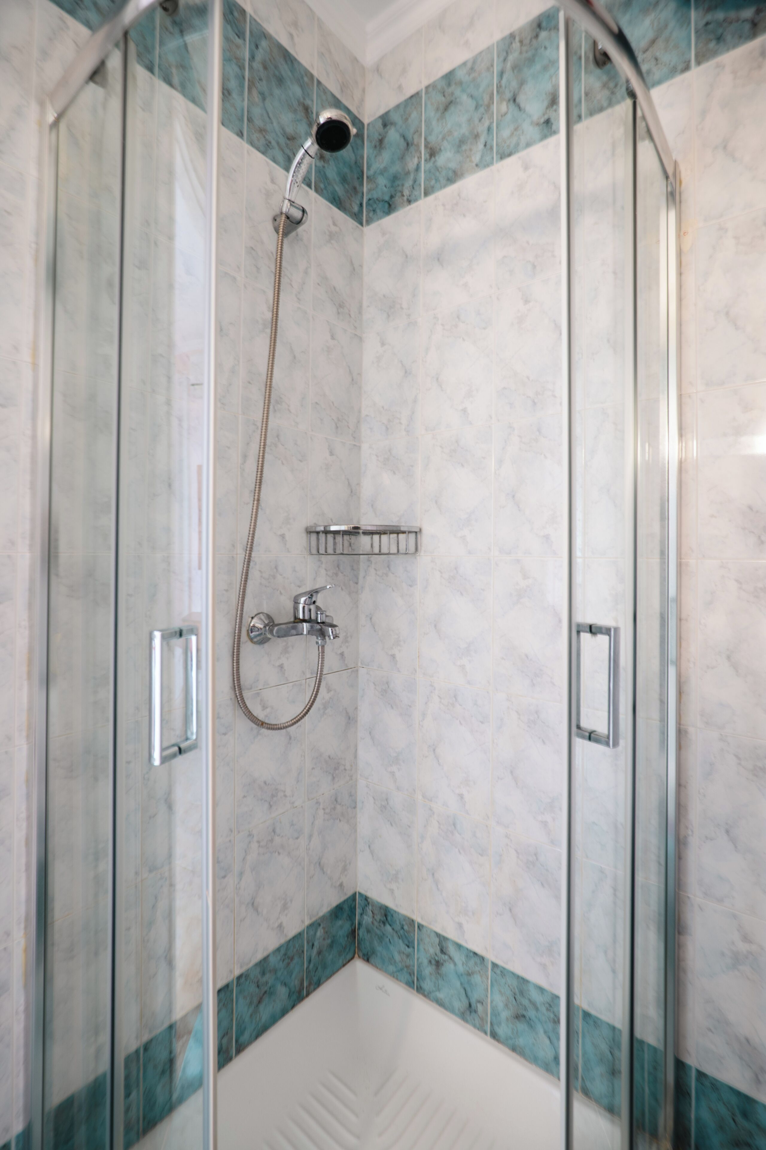 A glass-enclosed shower with a handheld showerhead and a wall-mounted faucet.