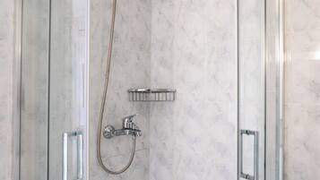 A glass-enclosed shower with a handheld showerhead and a wall-mounted faucet.