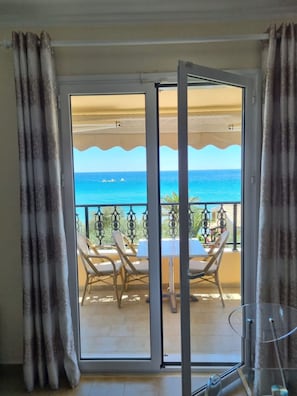 A room with a sliding glass door leading to a balcony with a table and chairs, overlooking the sea. - Corfu Glyfada Menigos Resort 40 (Corfu)