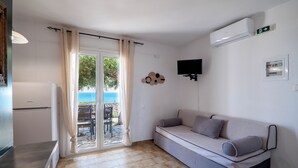 A room with a sofa, a television, an air conditioning unit, and a sliding glass door leading to an outdoor area. - Corfu Glyfada Menigos Resort 24 (Corfu)