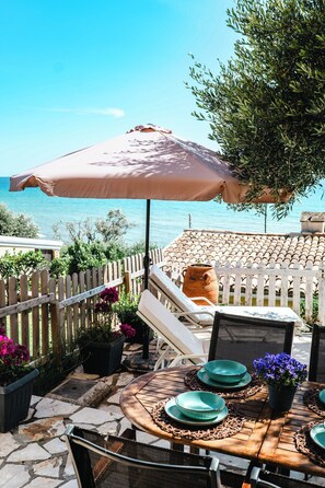 An outdoor patio with a table set for dining, a white fence, and a view of the sea. - Corfu Glyfada Menigos Resort 24 (Corfu)