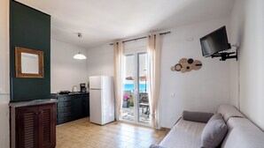A compact living space with a kitchenette, a sofa, a television, and a sliding glass door leading to an outdoor area. - Corfu Glyfada Menigos Resort 24 (Corfu)