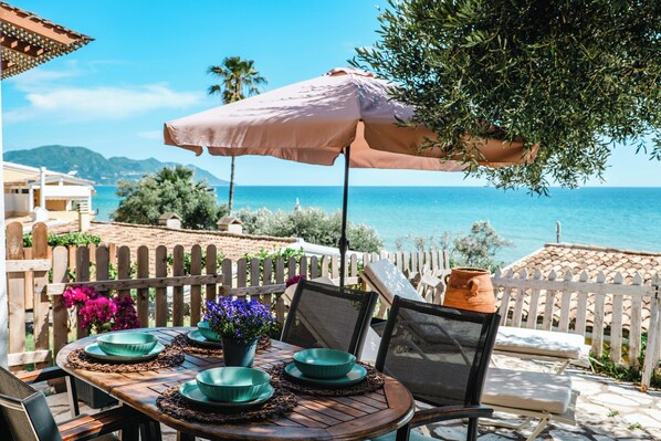 Una mesa dispuesta con cuencos verdes y una planta en maceta, con vistas a la costa, una cerca de madera y una cerca blanca con piquetes.