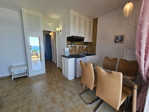 A compact kitchen with a coffee maker, a sink, and cabinets. There is a dining area with chairs and a table. - Corfu Glyfada Menigos Resort 2-5 (Corfu)
