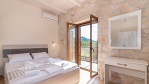Ein Schlafzimmer mit einer Steinsäule, einem großen Bett, einer Schiebetür zum Balkon und einem weißen Nachttisch.