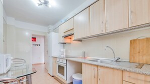 Et moderne køkken med indbygget ovn, vask og spiseplads med et glasbord og stole.