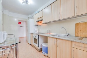 A modern kitchen with a built-in oven, a sink, and a dining area with a glass table and chairs. - Superior Beachfront Apartment with Pool, Balcony, Sea Views & Wi-Fi; Parking Available (Candelaria)