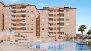 A multi-story residential building with balconies, a swimming pool, and a clear sky. - Superior Beachfront Apartment with Pool, Balcony, Sea Views & Wi-Fi; Parking Available (Candelaria)