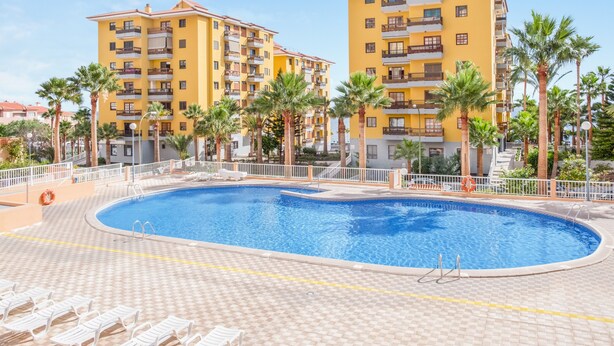 A hotel with a swimming pool surrounded by palm trees and a tiled deck. - Superior Beachfront Apartment with Pool, Balcony, Sea Views & Wi-Fi; Parking Available (Candelaria)