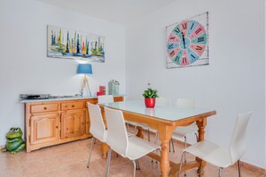 A dining area with a wooden table, white chairs, a clock, a painting, and a frog sculpture.