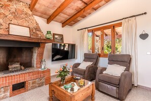 A living room with a stone fireplace, a flat-screen TV, two brown armchairs, and a wooden coffee table. - Fantastic Finca Son Mulet with Pool, Aircondition, Garden, Terrace & WLAN; Parking Available (Llubí)