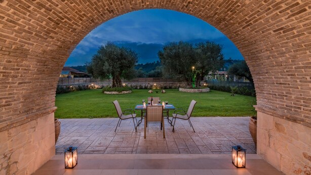An outdoor patio with a brick archway, a table set for dining, and a view of the landscape.