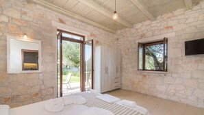 A bedroom with stone walls, a bed with white linens, a wooden ceiling, and a sliding glass door leading to an outdoor area.