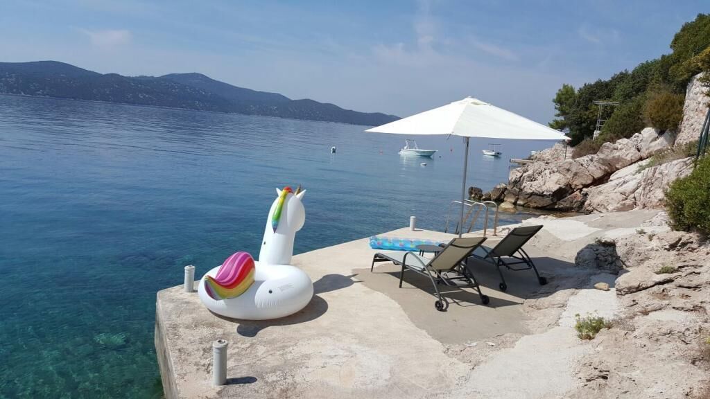 A seaside view with a concrete platform, lounge chairs, a white umbrella, and a decorative flamingo float.