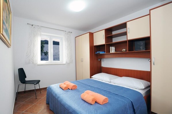 A bedroom with a bed, a chair, a window, and built-in storage cabinets. - Holiday Home Odiseja (Dubrovacko Primorje)