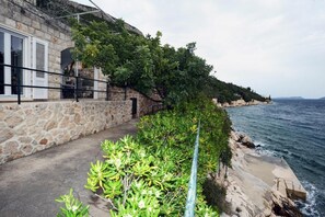 Un edificio costero con fachada de piedra, un balcón con barandilla metálica y vista al mar.