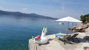 Vista al mar con agua cristalina, un flotador con forma de cisne blanco, sillas de descanso y una sombrilla.