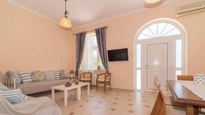 Una sala de estar con un sofá, sillas, una mesa, un televisor y una puerta con un ventanal de arco.