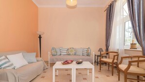 Un salón con un sofá, dos mesitas blancas y sillas de madera.