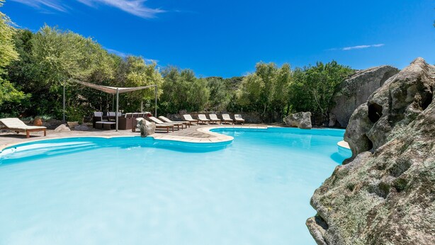 A swimming pool with lounge chairs, surrounded by trees and rocks. - Dream Villa with Terrace, Wi-Fi, Air Conditioning and Shared Pool (Porto Rotondo)