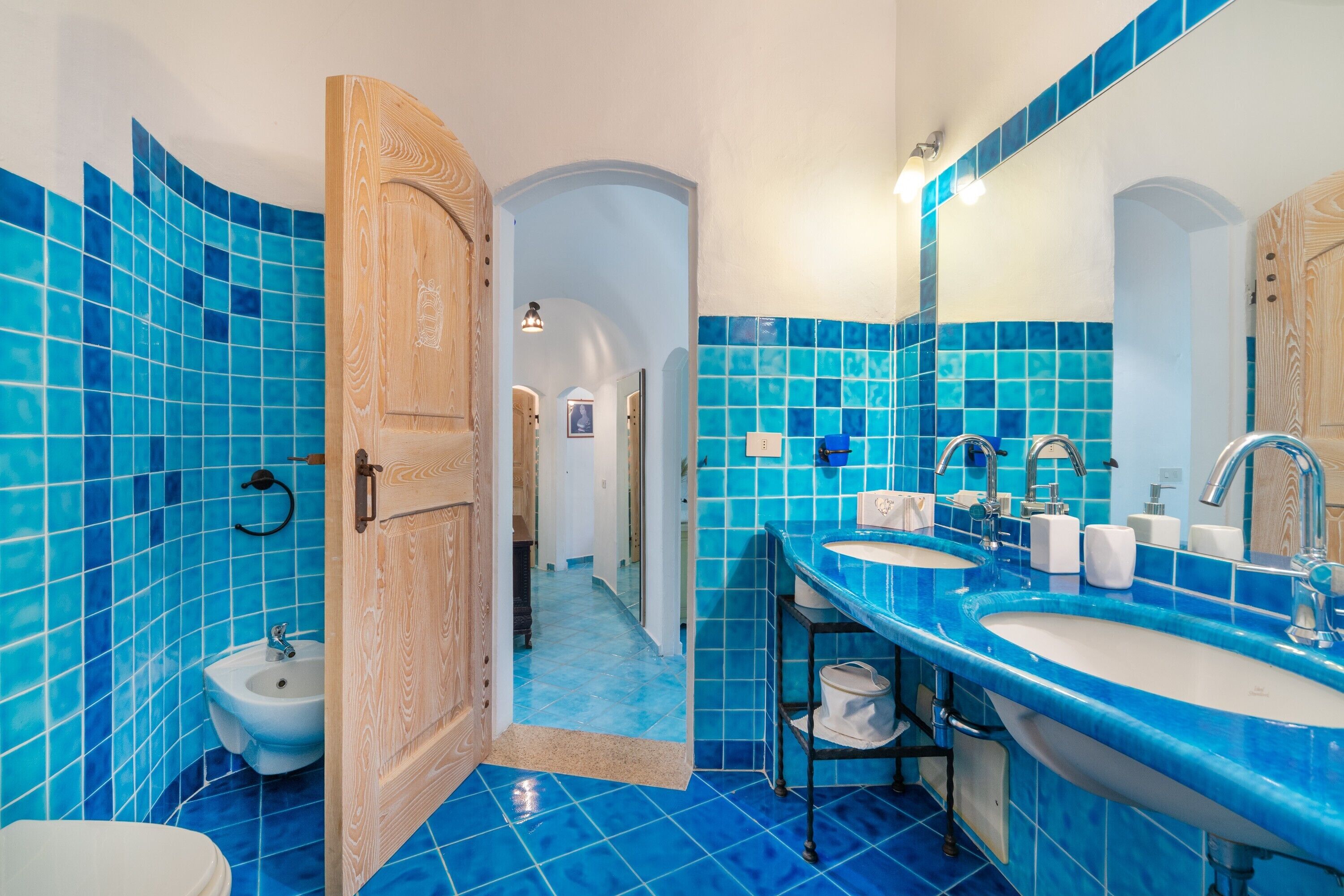 Une salle de bain avec des carreaux bleus, une porte en bois, un lavabo et un miroir.
