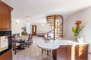Una cocina con armarios de madera, una mesa de comedor con sillas, una escalera de caracol y una sala de estar con un sofá.