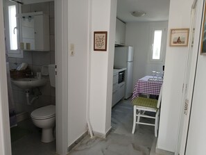 A compact kitchen with a refrigerator, oven, and a dining table with a checkered tablecloth. - Kiki's Dream Refurbished Apartment With a Bacony and sea Views (Paros)