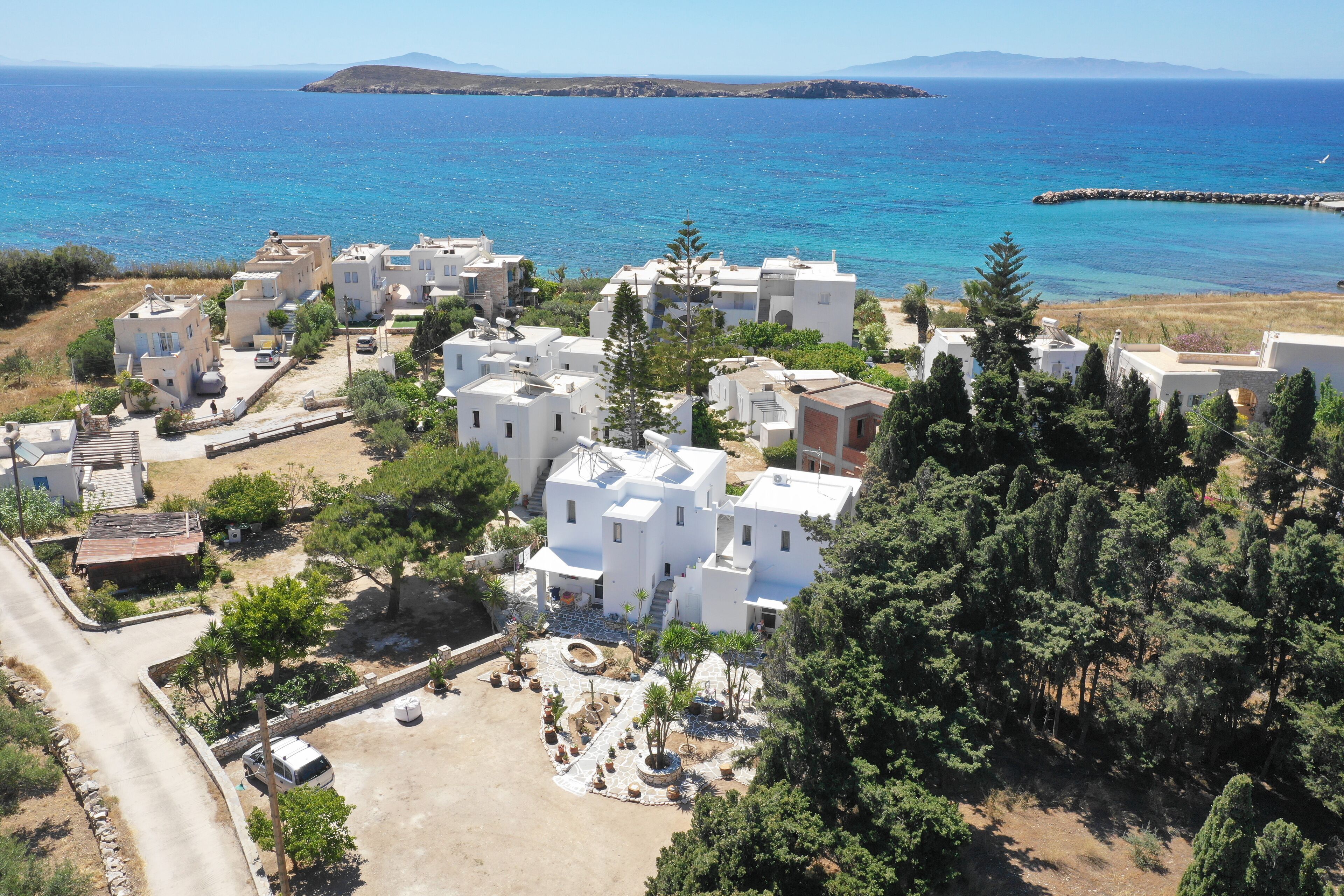 A coastal residential area with white buildings, a paved courtyard, and a view of the sea.
