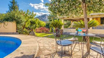Piscina com cadeiras e uma mesa, cercada por vegetação e uma montanha ao fundo.