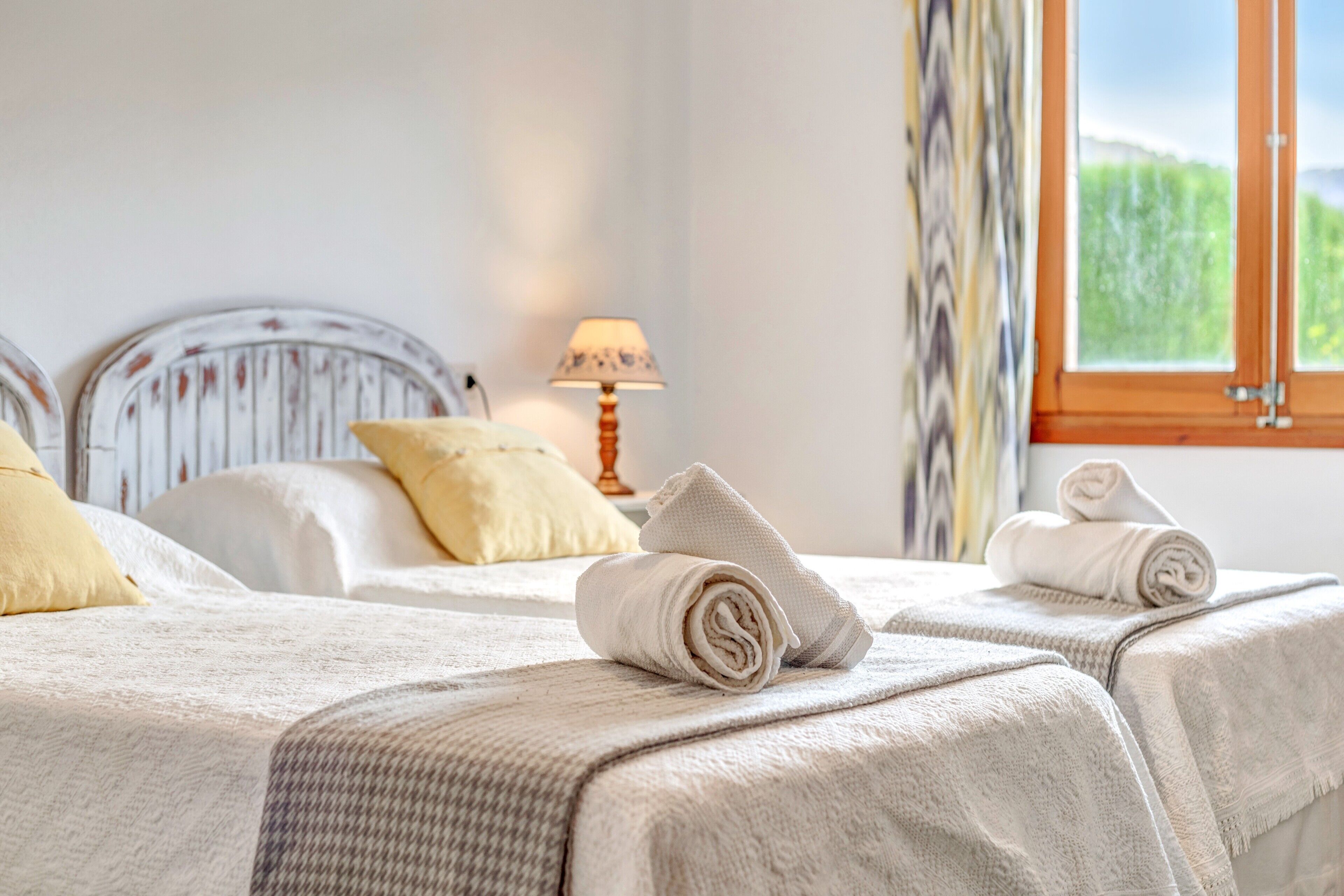 A hotel room with two beds, a lamp, and a window with a view of greenery.