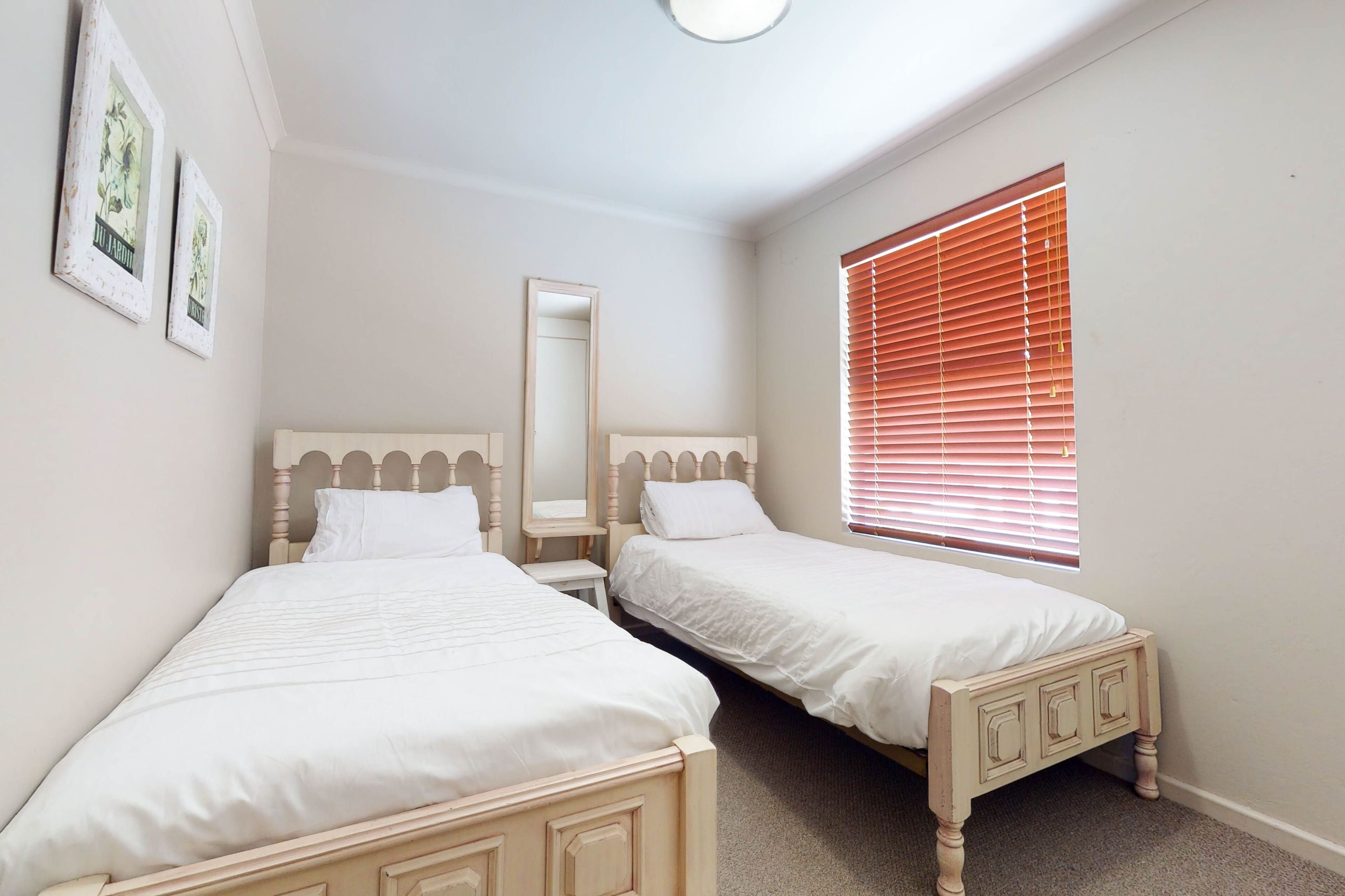 A bedroom with two single beds, a mirror, and a window with blinds.