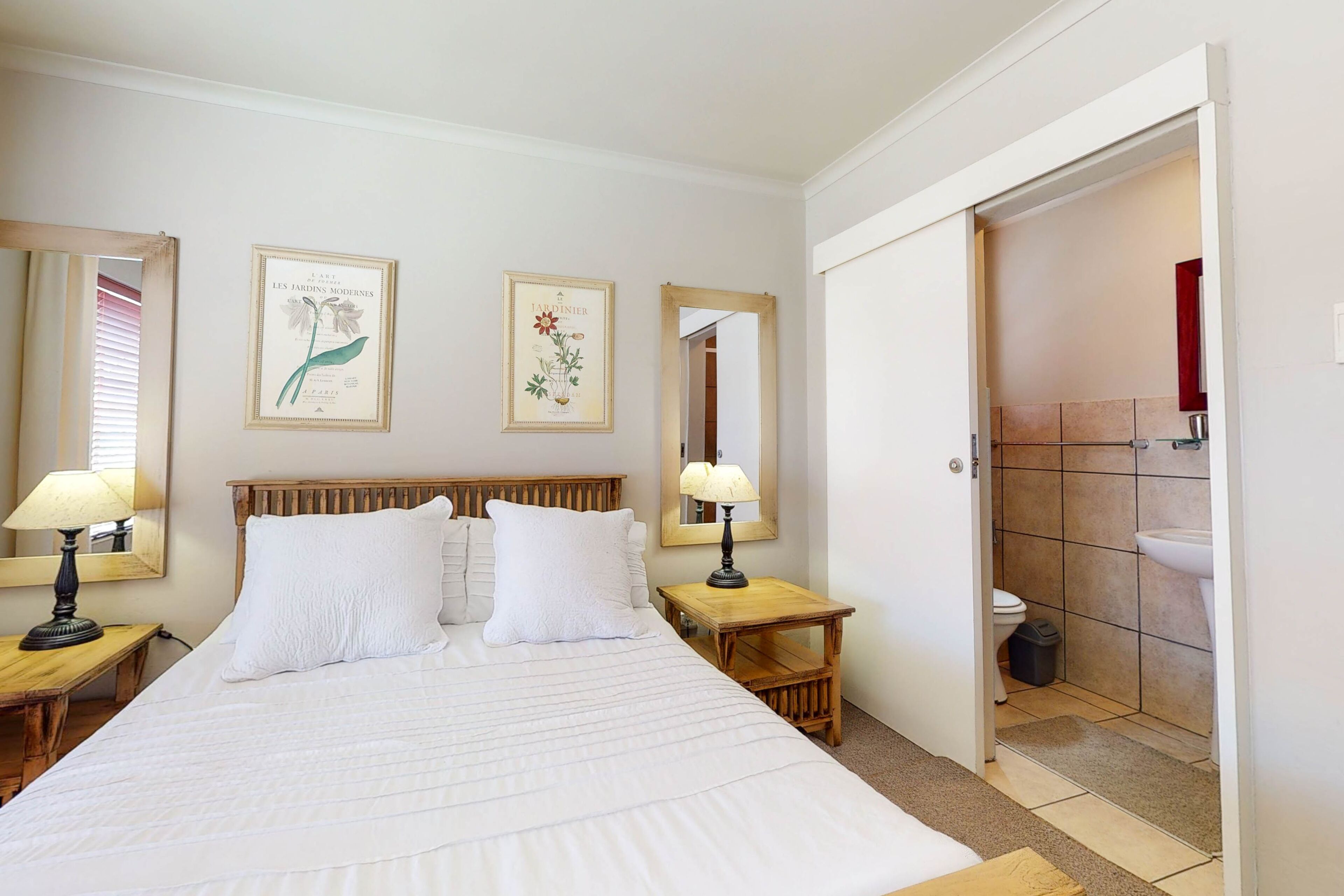 A hotel room with a large bed, two bedside tables with lamps, a wooden headboard, and two framed botanical prints on the wall.