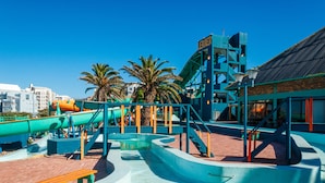 Un parc aquatique avec des toboggans et une piscine, entouré de palmiers et de bâtiments.