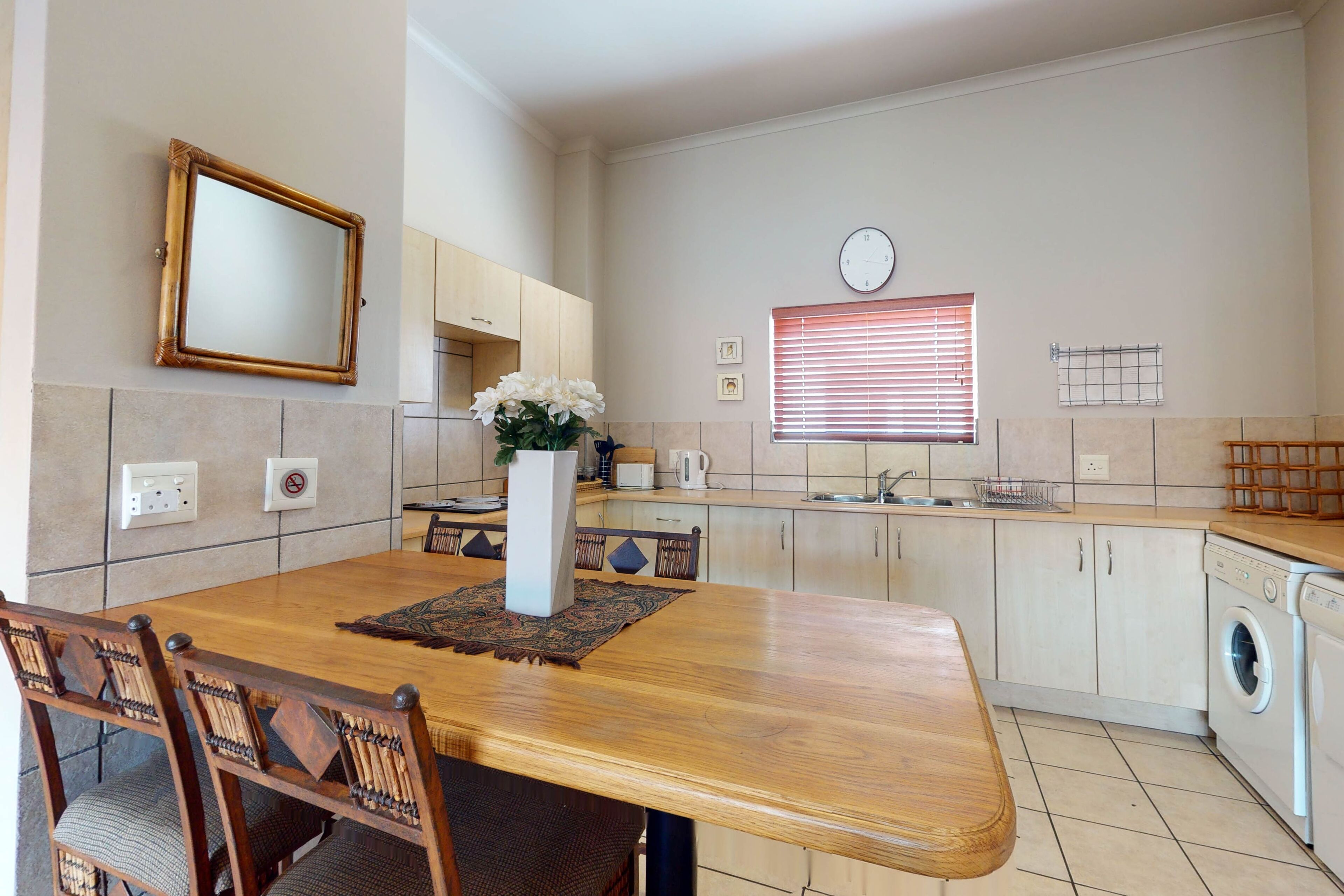 A modern kitchen with a wooden dining table, chairs, a built-in oven, and a washing machine.
