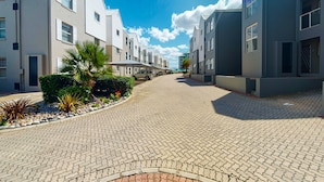 Une rue pavée bordée de bâtiments modernes, un ciel bleu azur et un palmier.