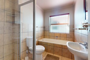 A bathroom with a glass shower enclosure, a toilet, a bathtub, and a sink. - Diaz Beach Villa (Mossel Bay)