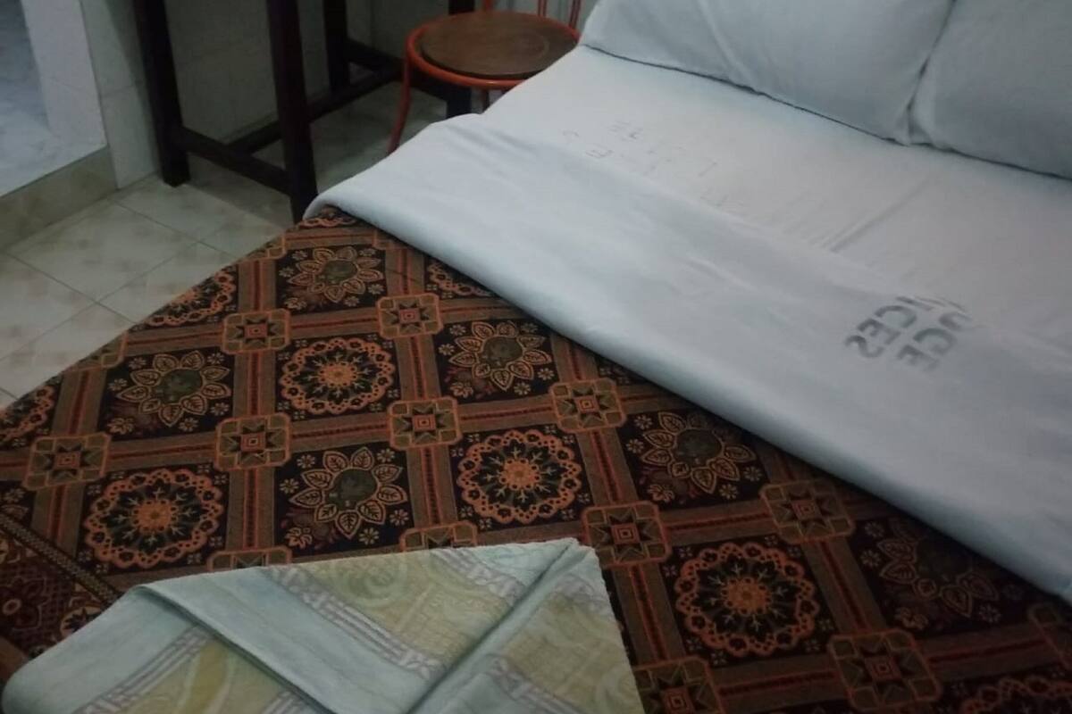 Una cama con ropa de cama estampada, una mesita con un rollo de papel higiénico y una silla.
