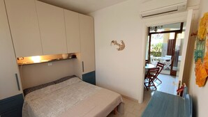 Un dormitorio con una cama, un escritorio y una silla. Hay una ventana y un equipo de aire acondicionado.