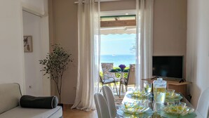 Quarto com sofá, mesa de jantar com cadeiras, televisão e vista para o mar.