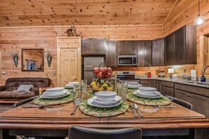 A wooden interior with a dining table set for four, kitchen cabinets, a refrigerator, and a microwave.