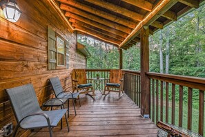 A wooden deck with chairs and a table, surrounded by a wooden railing, overlooking a forested area.