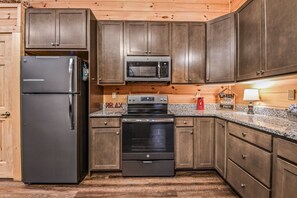 A kitchen with wooden cabinets, a stainless steel refrigerator, a microwave, and an oven. - Creekside On The Bluff 2 Bedroom Cabin by RedAwning (Sevierville)