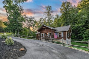 A rustic cabin with a porch, surrounded by a wooden fence and a gravel driveway. - Creekside On The Bluff 2 Bedroom Cabin by RedAwning (Sevierville)