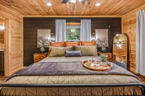 A cozy bedroom with a large bed, wooden walls, a window with curtains, bedside tables with lamps, and a tray with items on the bed. - Creekside On The Bluff 2 Bedroom Cabin by RedAwning (Sevierville)