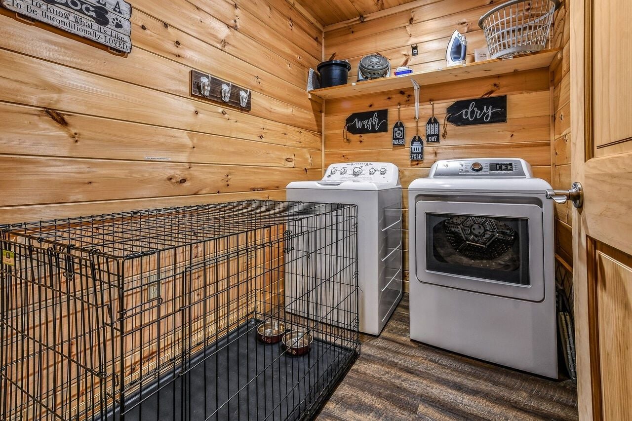 A compact laundry room with a washing machine, dryer, and a metal cage for pets.