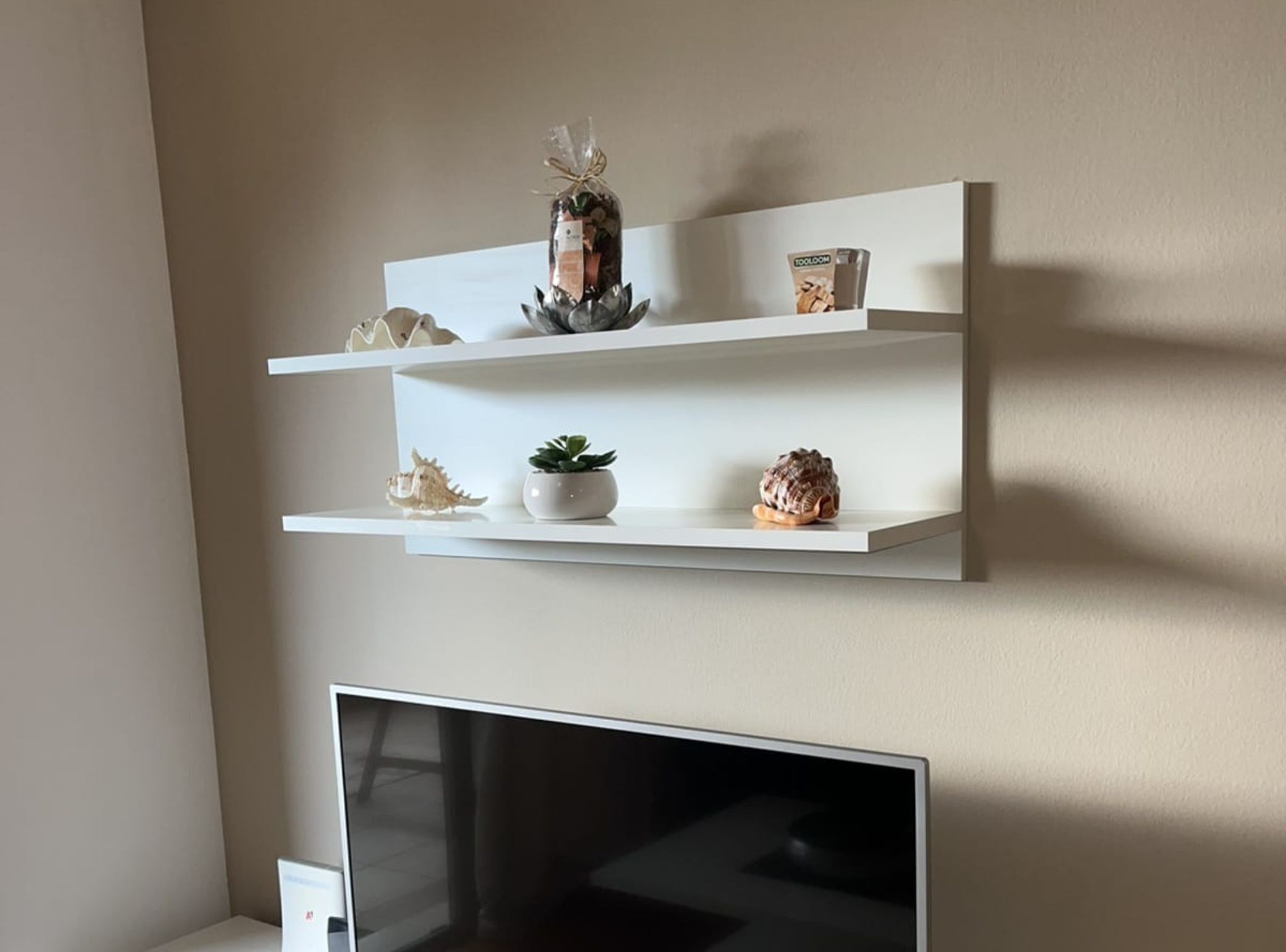 En vägghängd hylla med dekorativa föremål och en tv under.