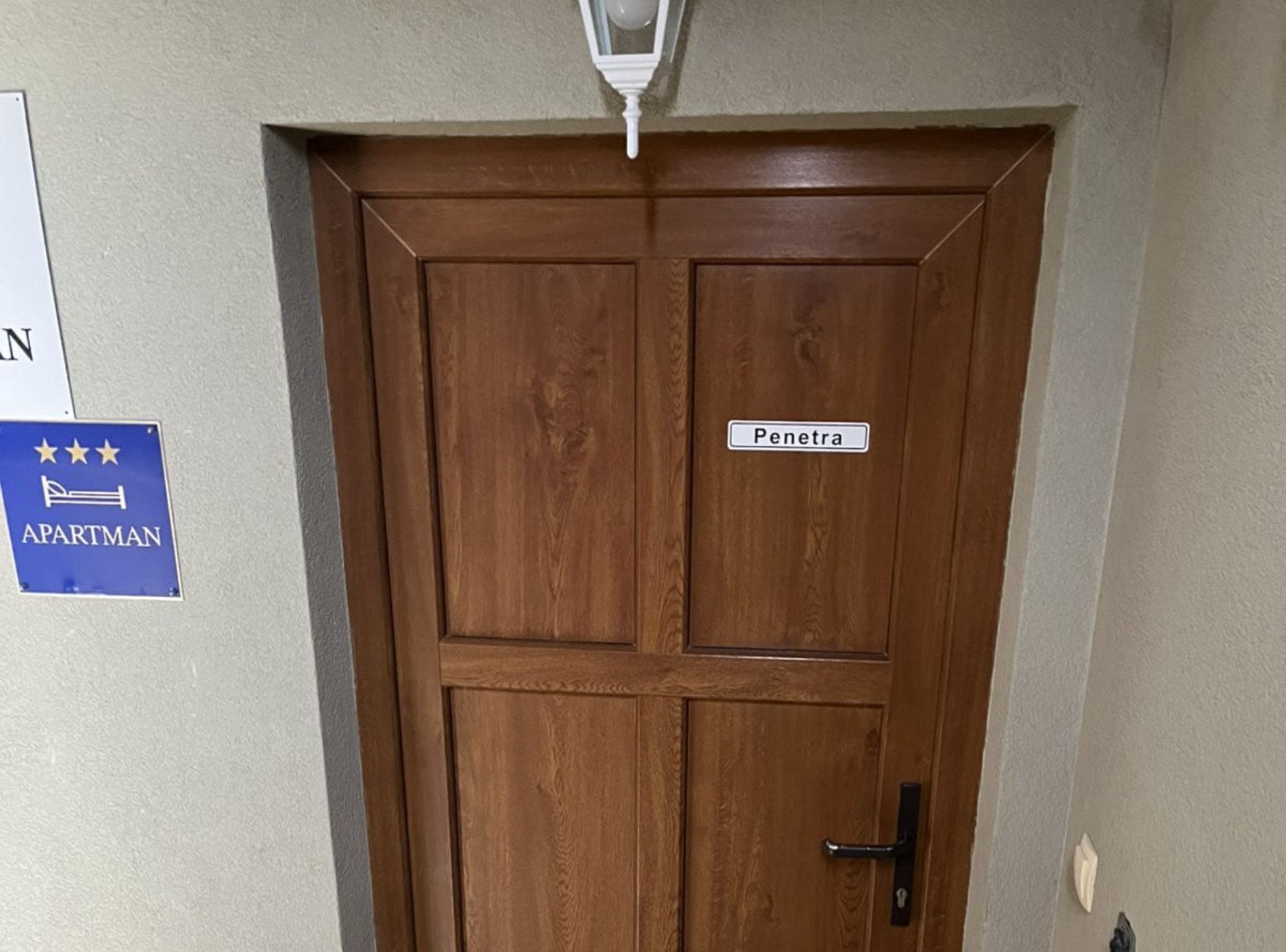 Une porte en bois avec une enseigne indiquant « Penetra », une enseigne bleue indiquant « APARTMAN », et un luminaire blanc au-dessus.