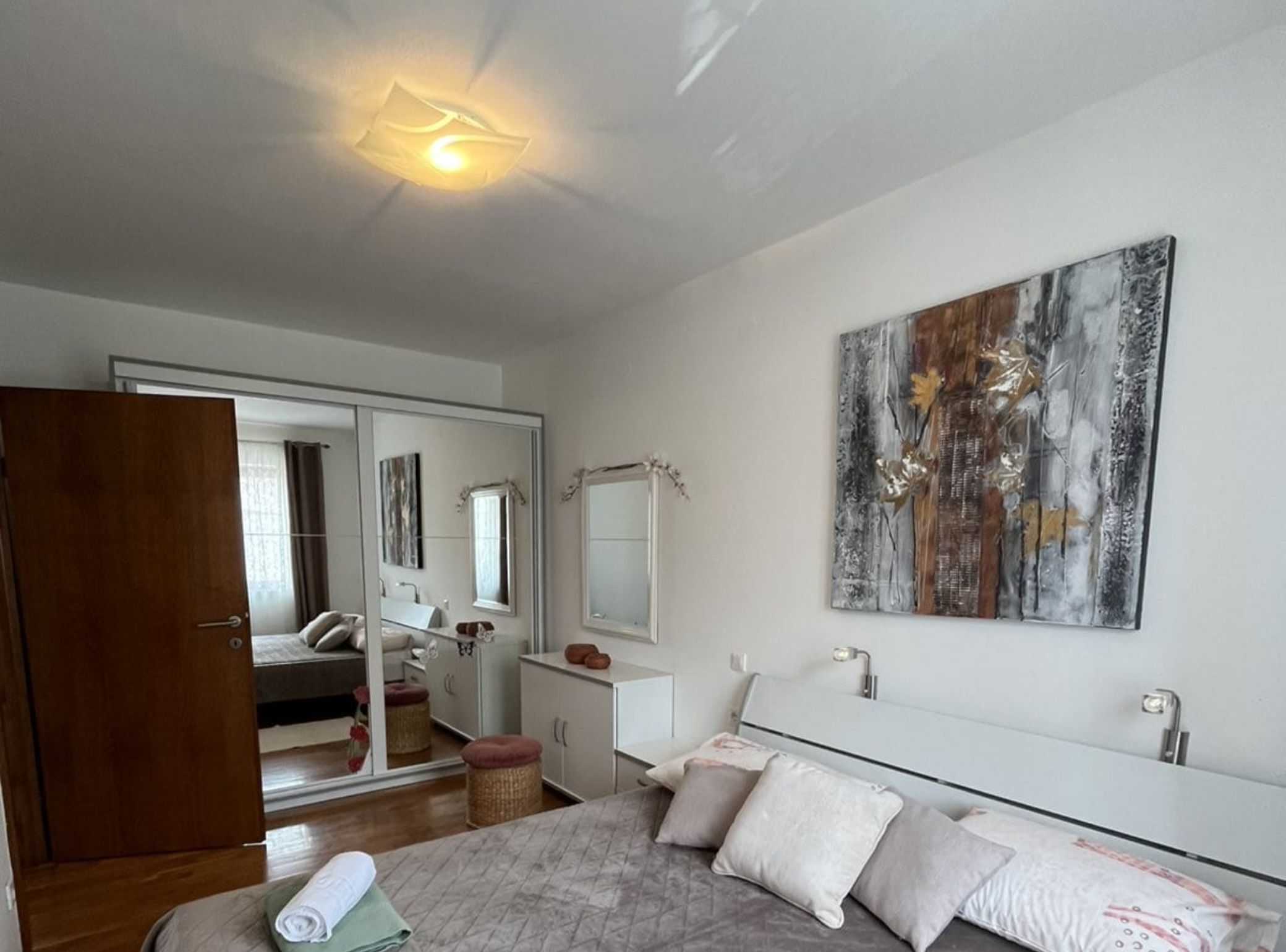 A bedroom with a bed, a bedside table, a mirror, and a large abstract painting on the wall.